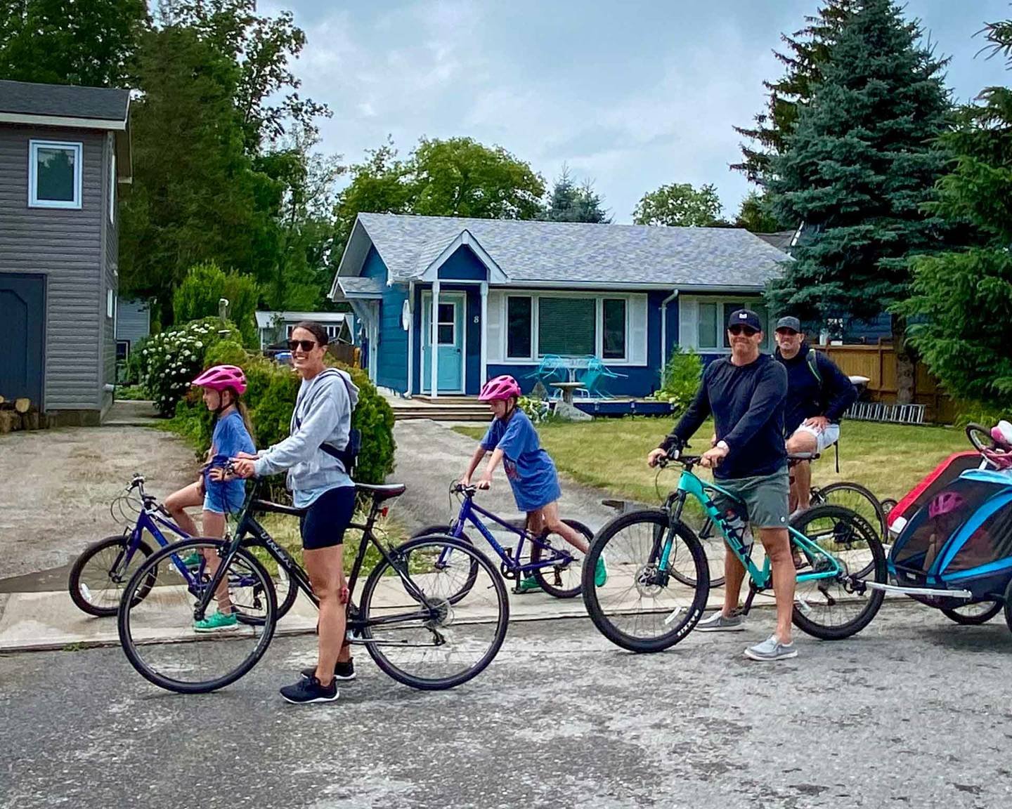 Two adults and two children on bikes, with a child trailer, setting off along a quiet residential street