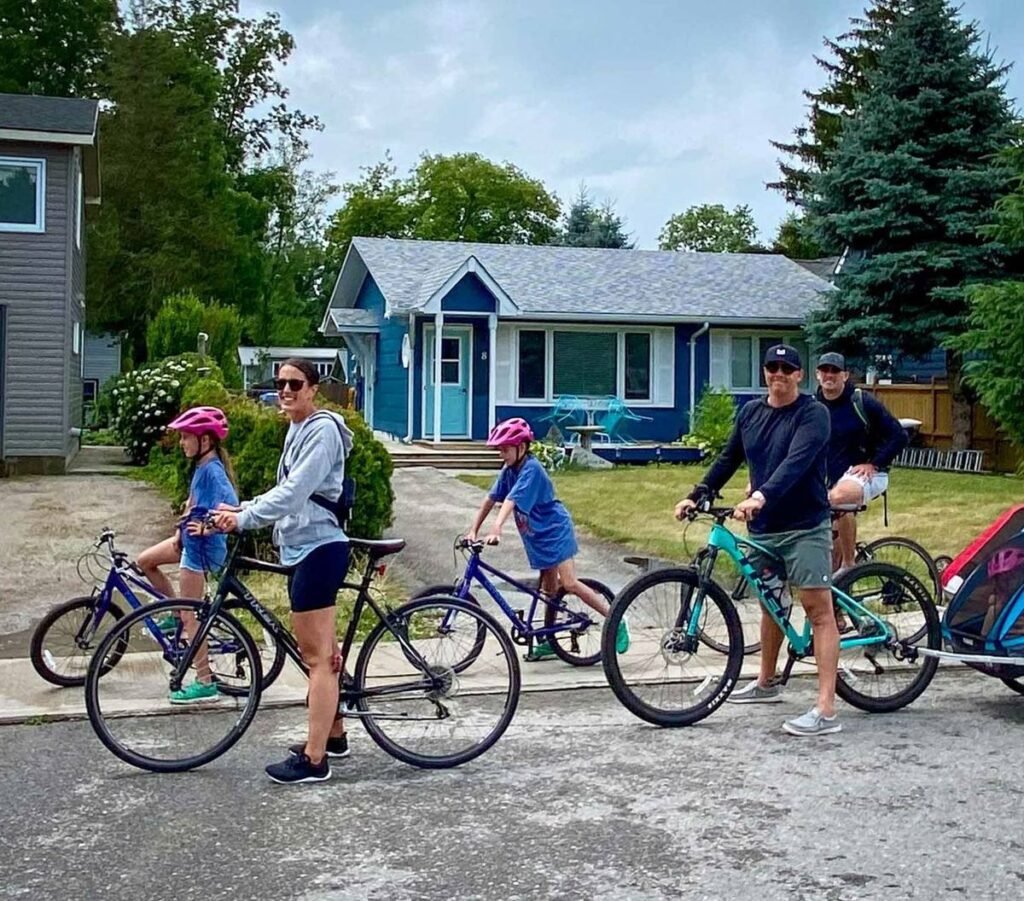 Two adults and two children on bikes, with a child trailer, setting off along a quiet residential street